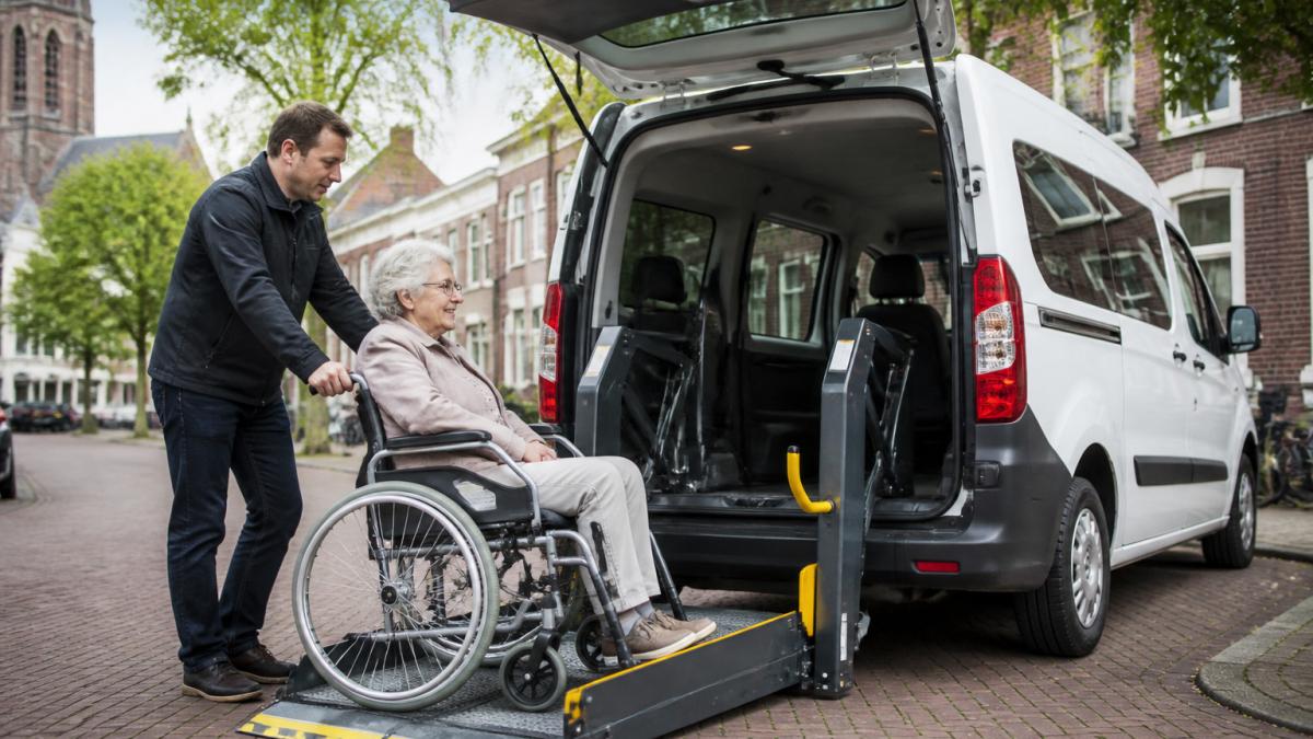 Een ervaren chauffeur helpt een oudere mevrouw in een rolstoel veilig instappen in een wit rolstoelvoertuig met automatische lift, op een rustige straat in Utrecht