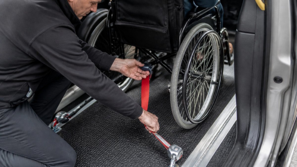 Chauffeur controleert de veiligheidsgordels van een rolstoel in een taxi met oprijplaat voor een veilige rit.