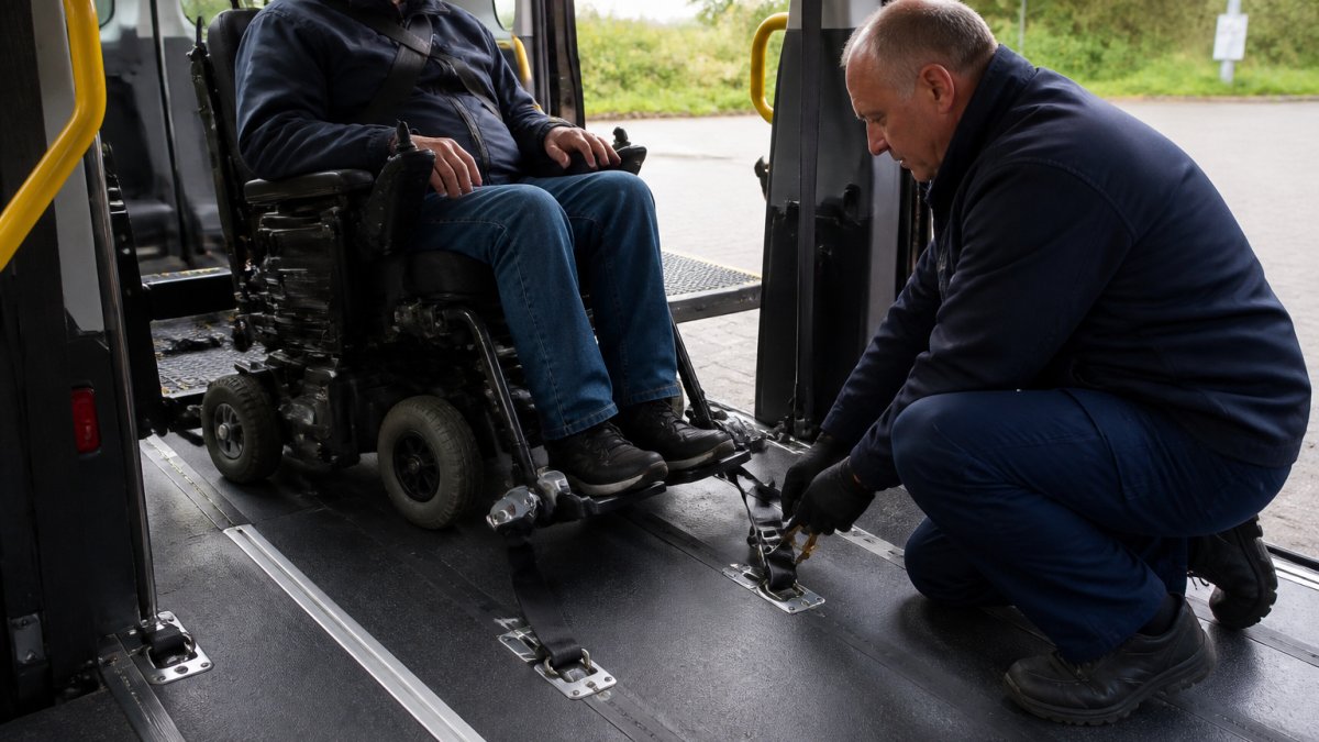 Chauffeur zet een zware elektrische rolstoel veilig vast met spanbanden in een toegankelijke rolstoeltaxi.