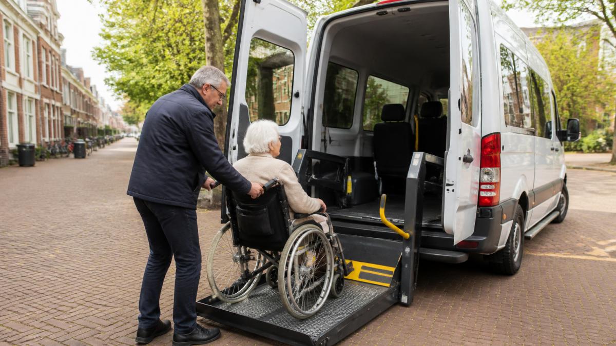 Chauffeur van taxicentrale Utrecht helpt dame in rolstoel bij het instappen in een toegankelijke taxi.
